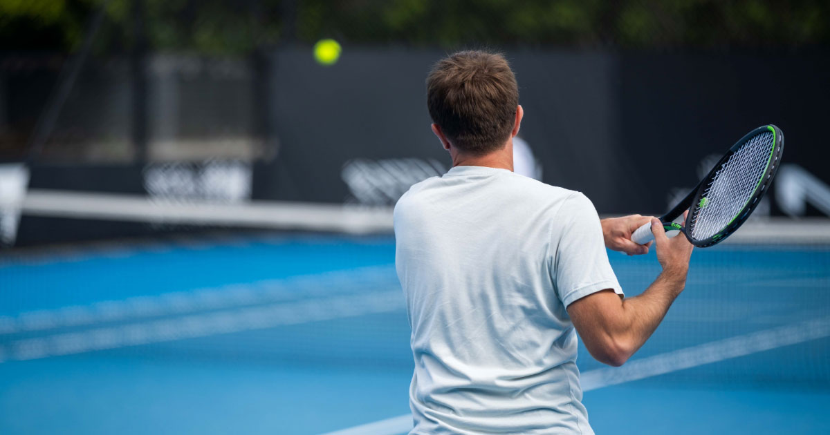 Man wearing white tennis gear returning shot on blue court