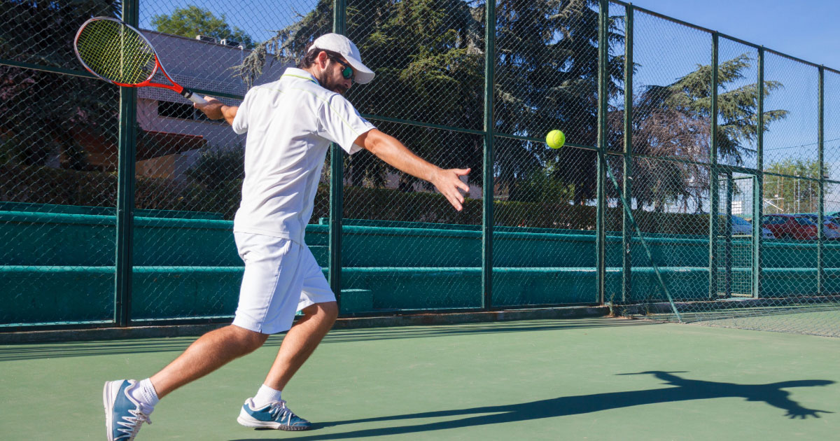 Young man wearing white hat, shirt, shorts, and shoes in his backswing preparing to hit a passing tennis shot