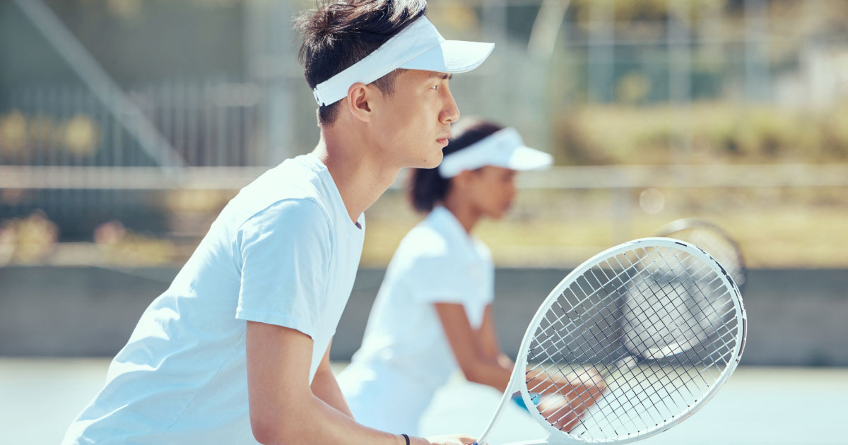 Young Asian male and black female tennis doubles partners preparing to receive their opponent's serve
