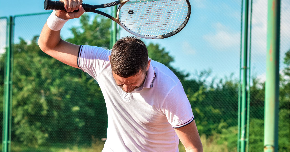 Male tennis player holding his racket up as though he's about to smash it on the ground in anger
