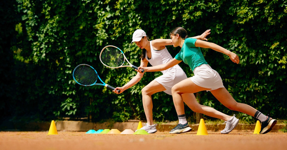 Two young women holding tennis rackets going through practice motions on court