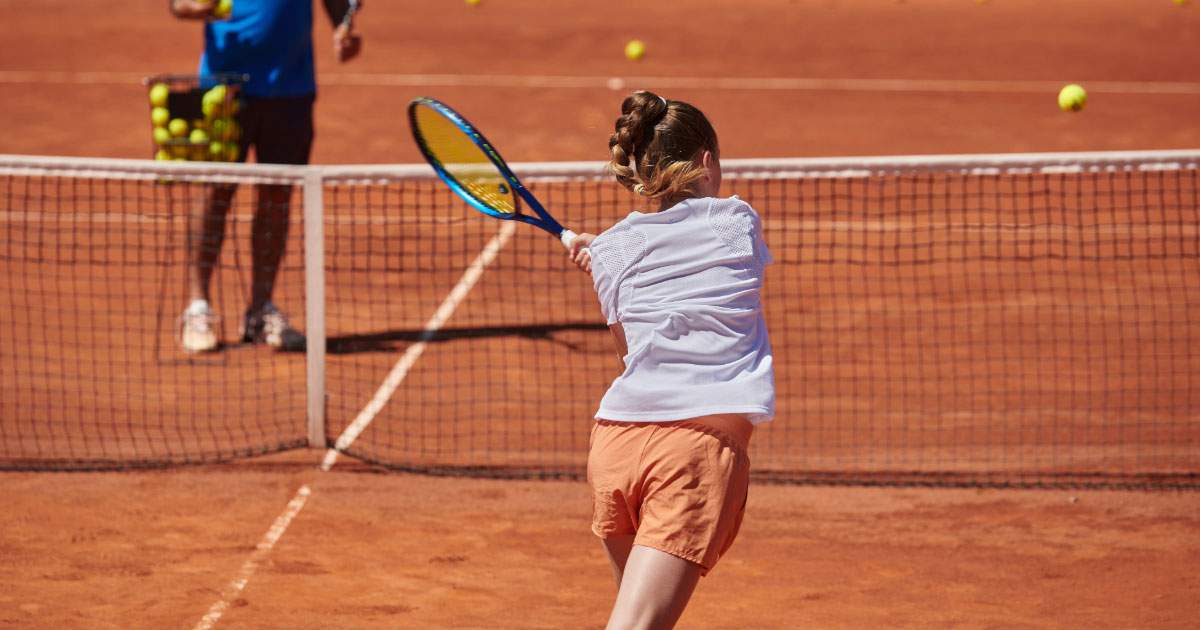 Coach doing forehand practice drills with young student on clay court